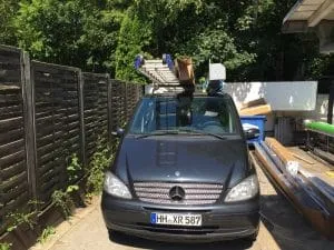 Ein schwer beladenes Auto mit verschiedenen Gegenständen auf dem Dach parkt draußen.