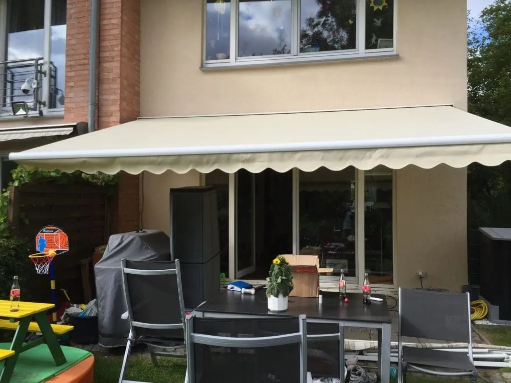 Ein Wohnhinterhof mit einer Toscana-Grande-Terrasse, überdacht von einer Markise, Möbeln, Kinderspielzeug und einem kleinen Basketballkorb.