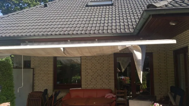 Terrassenbereich eines Backsteinhauses mit Markise, Gartenmöbeln und Gartenblick.