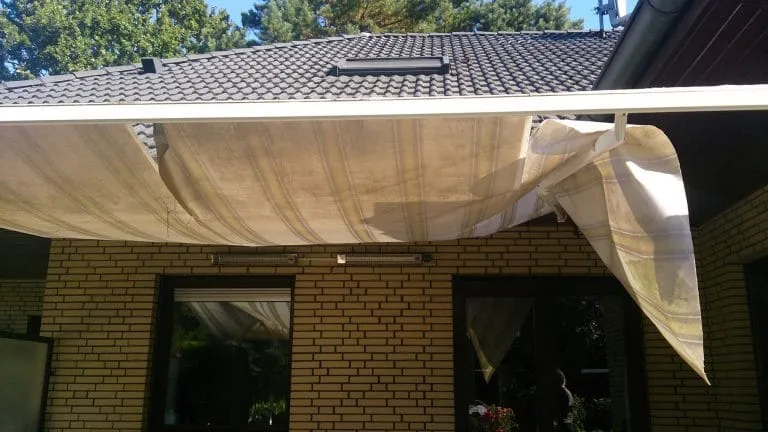 Beschädigte ausziehbare Markise an einem Backsteinhaus mit lose hängendem, zerrissenem Stoff.