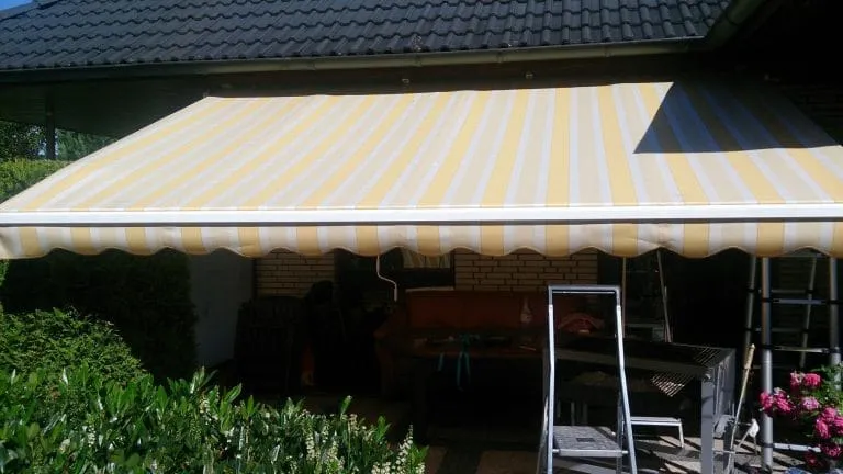 Gestreifte Markise erstreckt sich über einen Terrassenbereich mit Gartenmöbeln.